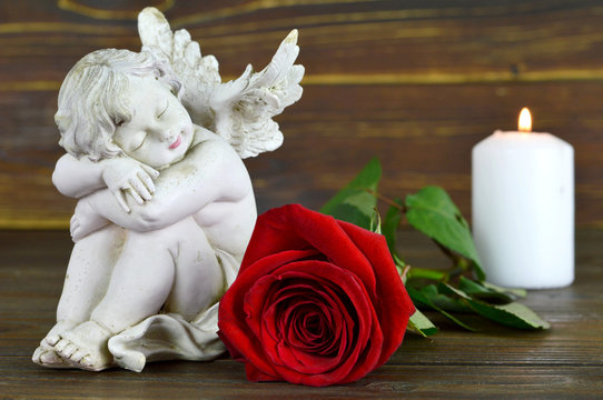 Condolence card with an angel, red rose and white burning candle on wooden background