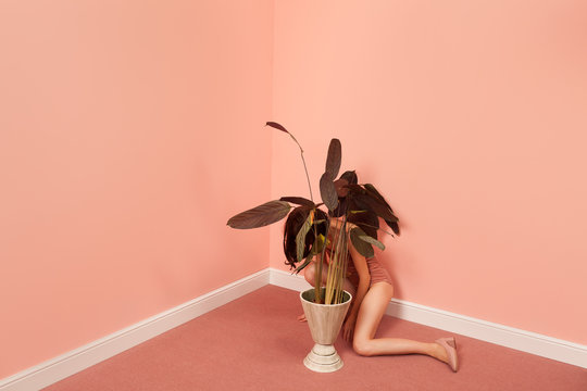 woman in a pink room hiding behind a plant