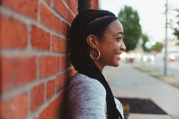 A young african american woman leaning against a brick wall