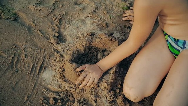 Little boy playing on the beach in the sand. Child sculpts figures out of the sand. Activities in the summer on the sea.