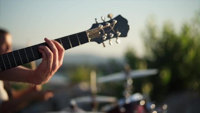 close up shot of the rhythm of the guitar, the men's hands touch the strings and get an energetic melody outdoors during the day, the person holding the mediator