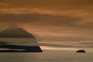 Naklejka na ściany i meble Sunset in the Islands of Southeast Alaska. Low hanging clouds make for a picturesque and atmospheric environment during a dramatic sunset in the islands of southeast Alaska.