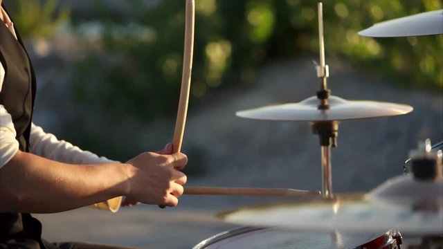close up shot of the men's hands, who holds the drumsticks in their hand, the people energetically hit them on the plates in the daytime outside, maybe this is a street musician
