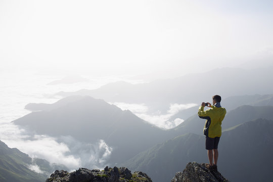 Young man taking a photograph of the scenic view from the top of a mountain