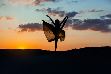 Obraz premium Dancer at sunset against the sky, her dress fluttering. The backlight of the sun only contours of the figures are visible.