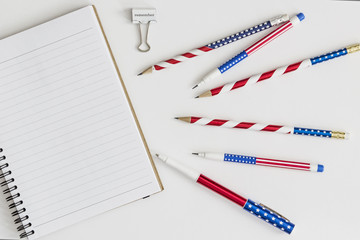 Blank notebook, stars and stripes pens and pencils and paper clip saying "remember"