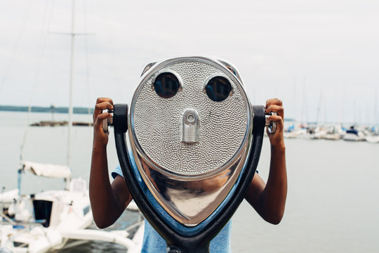 Black girl looking through binoculars by a bay