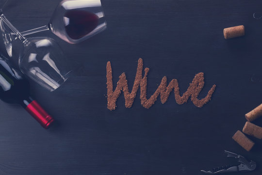 Bottle of red wine and two wine glasses on table with wine word letters, retro toned