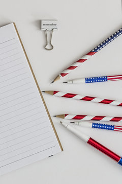 Blank notebook, stars and stripes pens and pencils and paper clip saying remember"""lank note"