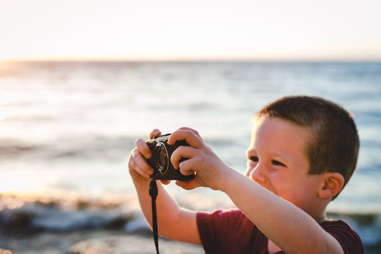 Young boy taking digital photos by a lake