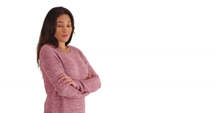 Portrait of young Latina woman in cozy pink sweater smiling at camera with arms crossed on white background. Attractive female looking at camera with friendly expression in studio with copyspace. 4k 