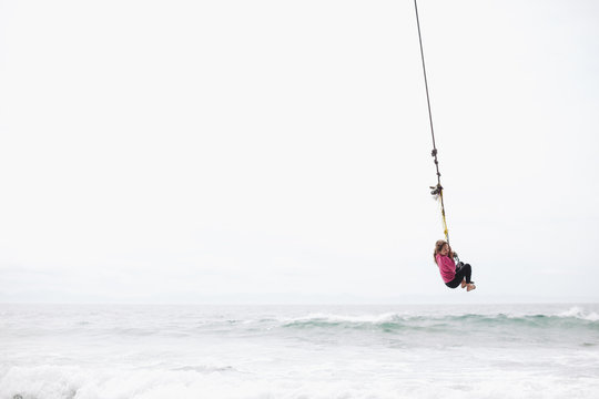 Young girl flying over ocean water on rope swing