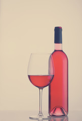 High glass with still rose wine and wine bottle, retro toned