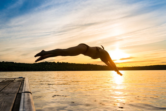 Woman Diving Off Dock Into Warm Summer Cottage Lake At Sunset