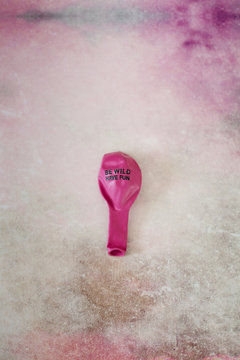 Still life of flat pink balloon and words Be wild, have fun printed on it