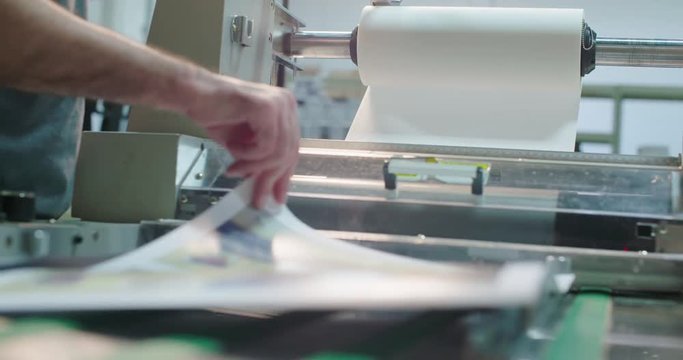 Worker Runs a Laminator Machine. a close up of a worker placing paper into a laminator machine
