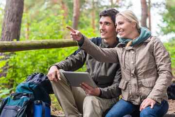 Woman and man hiking in woods determinating their position by GPS on tablet PC