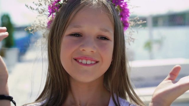 Portrait of cute girl with flower's crown smiling at camera on the bay bar. 4K