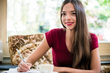 Young woman looking at camera while writing indoors in cafe