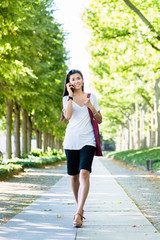 Obraz premium Young Asian woman talking on mobile phone outdoors in the park