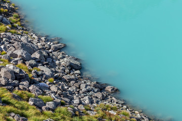 le bord d'un lac émeraude avec des rochers gris et de l'herbe verte