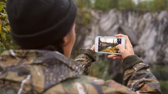Hiker woman in rain jacket taking picture with her smartphone outdoors. Female using mobile phone app to take photos with mountain view. 4K Slowmotion.