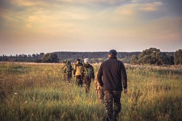 Groupe de personnes d& 39 affilée s& 39 en allant à travers champ rural au coucher du soleil pendant la saison de chasse à la campagne