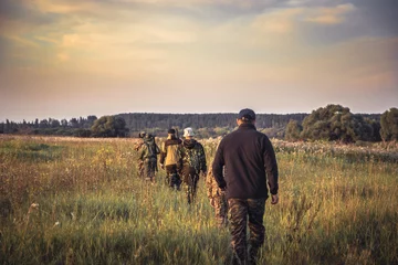 Papier Peint photo Lavable Chasser Groupe de personnes d& 39 affilée s& 39 en allant à travers champ rural au coucher du soleil pendant la saison de chasse à la campagne