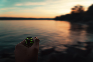 Eine Hand mit Bier vor einem See mit Sonnenuntergang