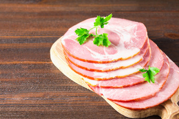 Sliced ham with fresh green lettuce leaves on a round cutting board. Meat products on a brown wooden table.