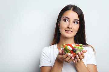 Young woman with vegetable salad in glass bowl on grey background