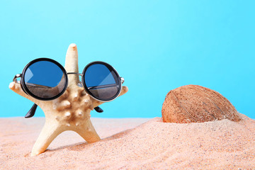 Fototapeta na wymiar Coconut with starfish in sunglasses on the beach sand