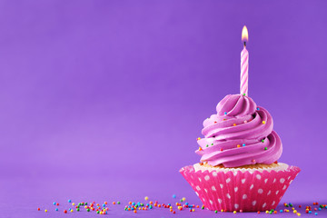 Tasty cupcake with candle on a purple background