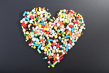 Colorful pills in shape of heart on black background