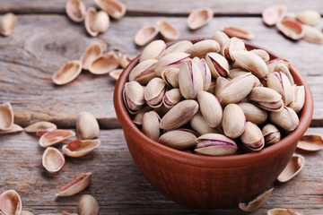 Heap of pistachios in bowl on wooden table