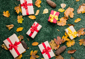 Holiday boxes with autumn leaves on green grass background.