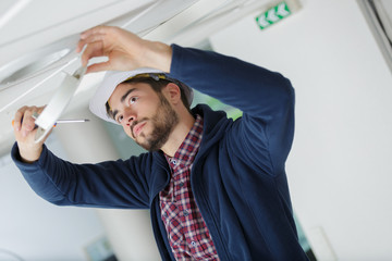 male electrician with screwdriver repairing fire sensor