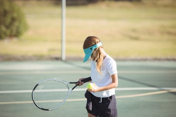 Girl holding tennis ball and racket on court