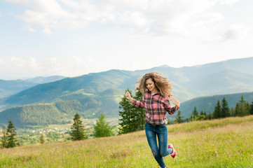 Curly young woman enjoying the view in the top of mountain on a hot summer day. Lifestyle concept