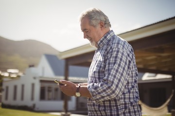 Senior man checking his mobile phone outside his house.