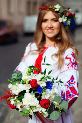 bouquet in focus in hands of  blurred girl in traditional ukrainian clothes