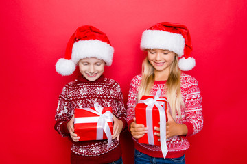 Small adorable charming relatives in traditional x mas clothing, isolated on red background, excited, looking at gifts, hold them and guess what`s inside, curiousity, wish, dream, imagination concept
