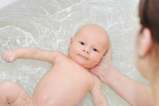 Caucasian woman is holding her newborn baby on the water while he bathing