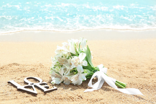 Beautiful bouquet and word LOVE on sand. Beach wedding concept