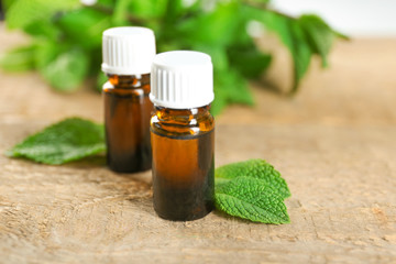 Bottles of essential oil and mint on wooden table