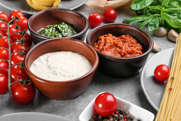 Delicious pesto, bolognese and white sauces for pasta in bowls on table