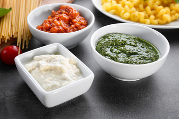 Delicious pesto, bolognese and white sauces for pasta in bowls on table