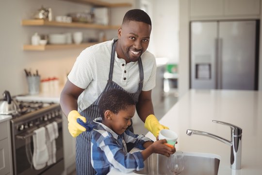 Smiling father and son cleaning cup in kitchen