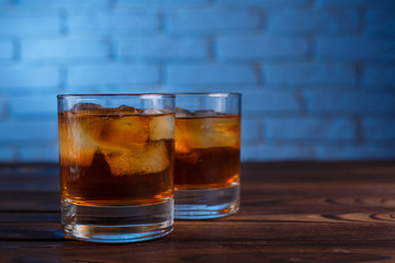 Whiskey with ice cubes on wooden table on brick wall background, copy space. Alcohol drinks, bar concept