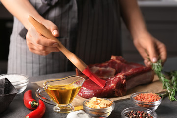 Woman applying oil onto raw steak with silicone brush in kitchen